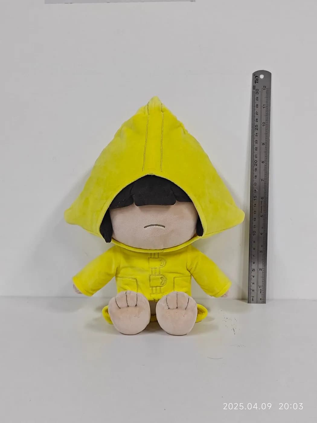 Cotton doll in a yellow hooded raincoat, measured against a steel rule