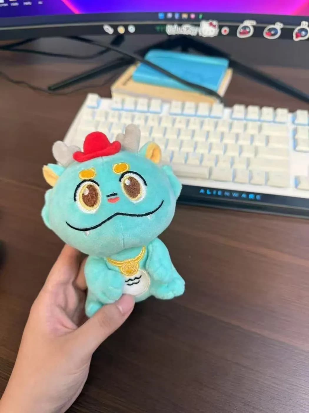 Teal dragon plush charm held above a keyboard
