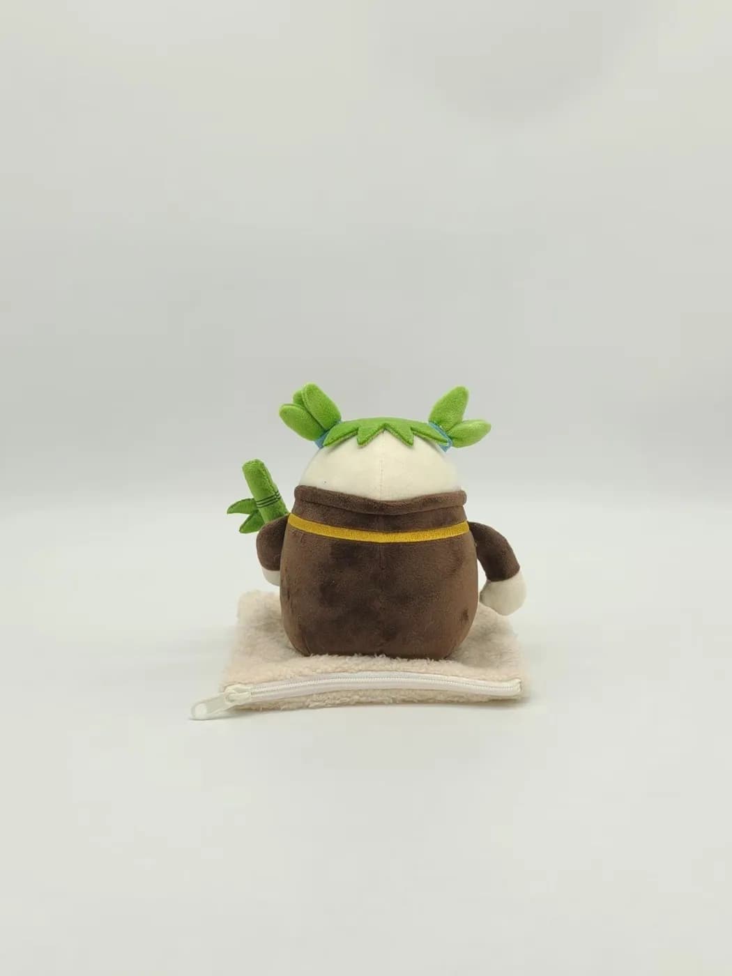 Pot character plush charm with felt sprouts, shown on a woven mat
